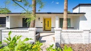 A modern two-story house with a yellow door, white brick walls, and a small porch area.