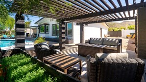 A covered outdoor patio with wicker furniture, a pool, and a view of a house in the background.