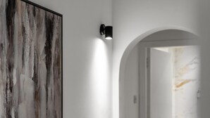 Un baño moderno con un cuadro abstracto grande, una lámpara de pared y una pared de mármol.