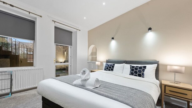 Una habitación de hotel moderna con una cama grande, una mesita de noche con lámpara, una ventana con vistas y un radiador.