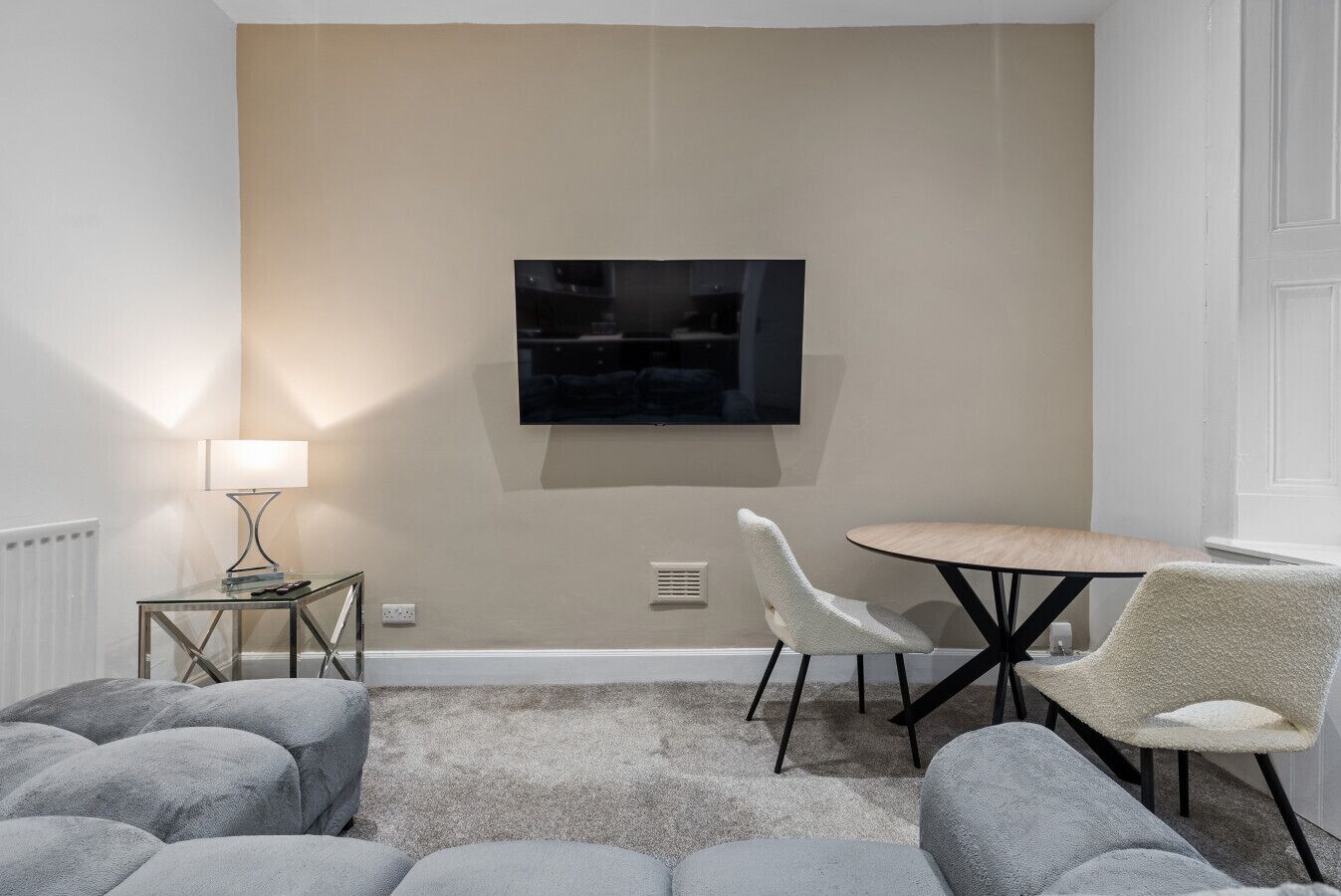 Een moderne woonkamer met een flatscreen televisie aan de muur, een ronde tafel met stoelen en een bank.