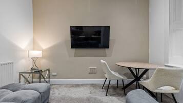 Een moderne woonkamer met een flatscreen televisie aan de muur, een ronde tafel met stoelen en een bank.