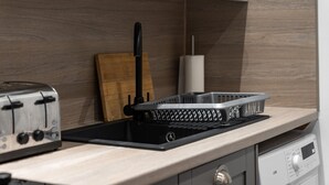 Una cocina con un tostador, una estufa eléctrica negra, una tabla de cortar de madera y un dispensador blanco de toallas de papel.