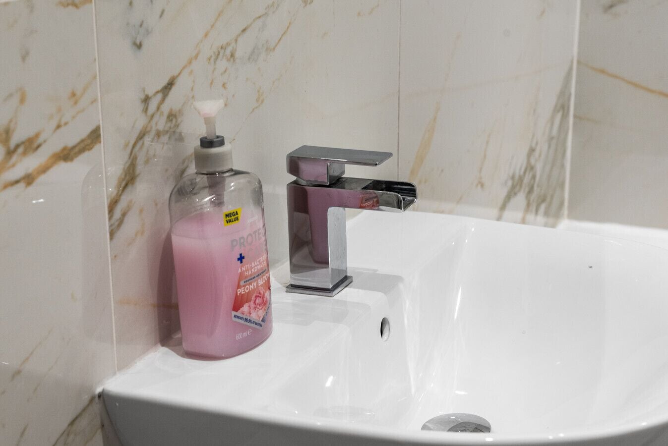 Une salle de bain avec un lavabo blanc, un distributeur de savon et un robinet.