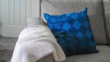 A grey sofa with a blue quilted pillow and a white knitted throw.