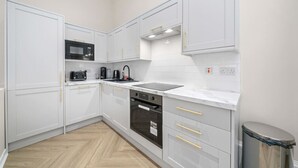 Una cocina moderna con armarios blancos, un microondas negro, una cafetera y un lavabo de acero inoxidable.