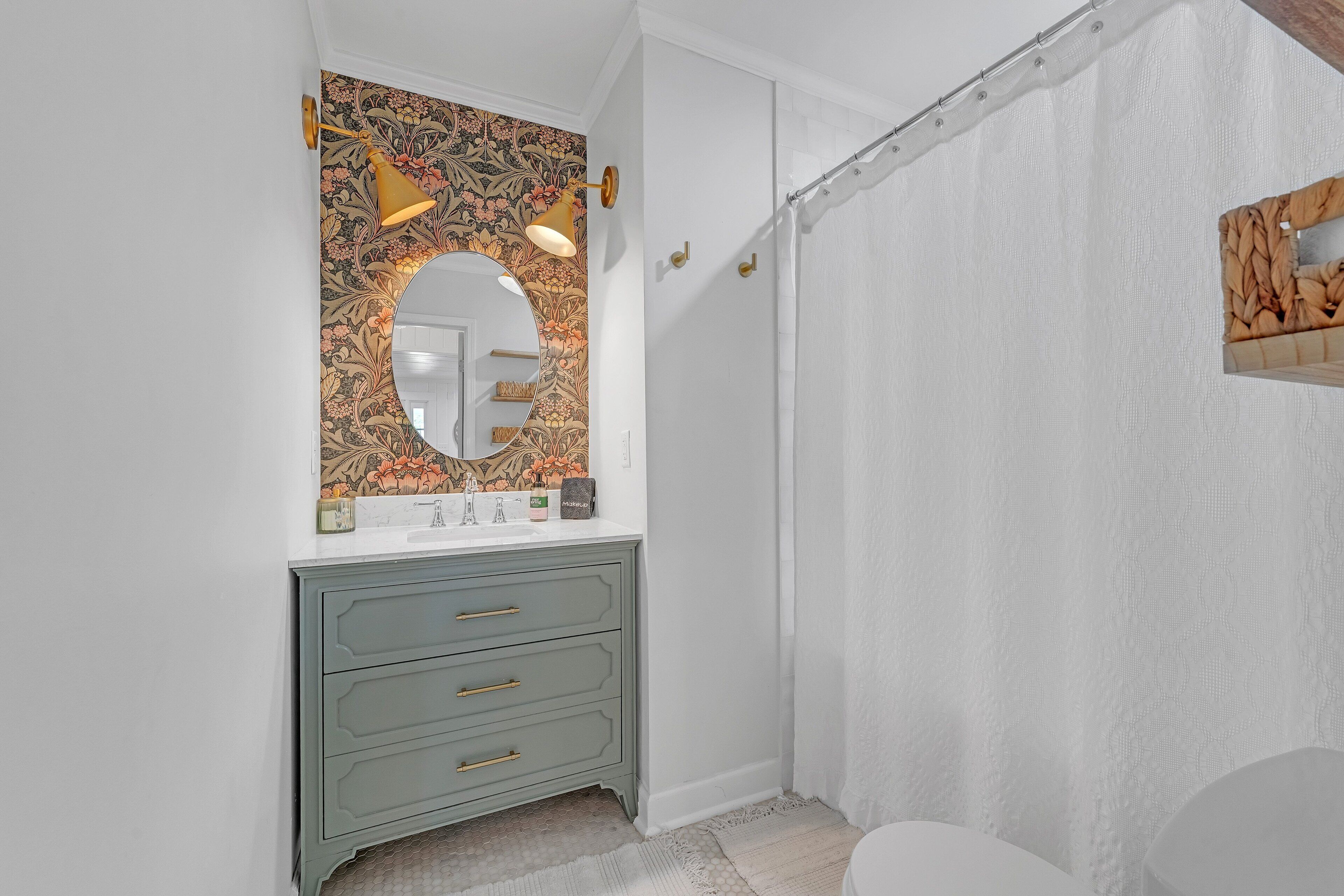 Een badkamer met een ronde spiegel, een lamp, een wastafel met lades, een douchegordijn en een toilet.