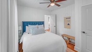 A bedroom with a bed, a ceiling fan, a bench, and a door. - Bungalow Off Floyd St In The Heart Of Covington 3 Bedroom Bungalow (Covington)