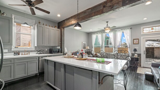 A modern kitchen with grey cabinets, a large island, and a dining area with a sofa and table. - The Sells House 3 Bedroom Home (Galveston)