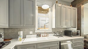 A modern kitchen with grey cabinets, a white countertop, a stainless steel dishwasher, a microwave, and a window above the sink. - The Sells House 3 Bedroom Home (Galveston)
