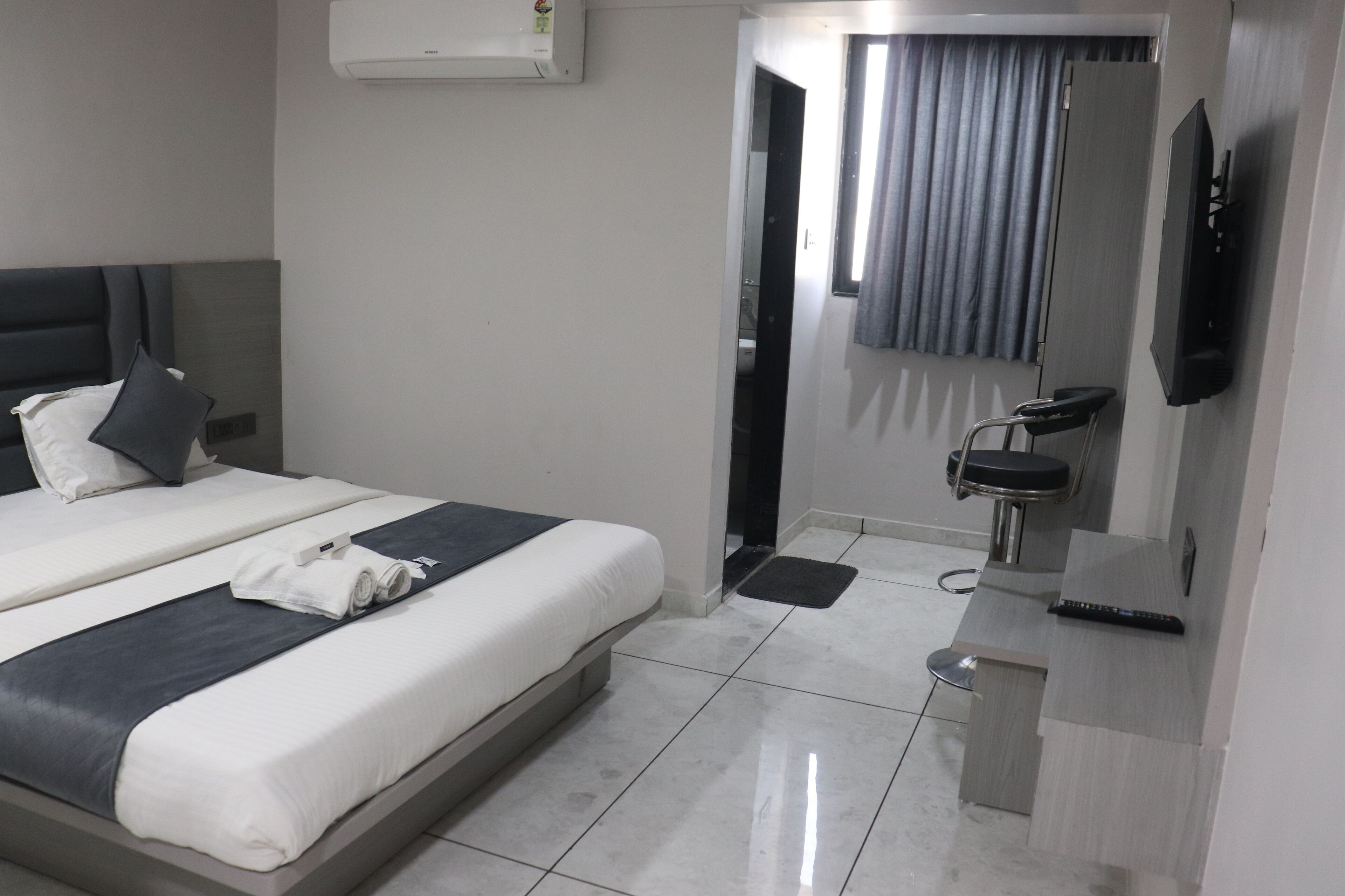 A modern hotel room with a bed, a desk, a chair, a TV, and a mirror.