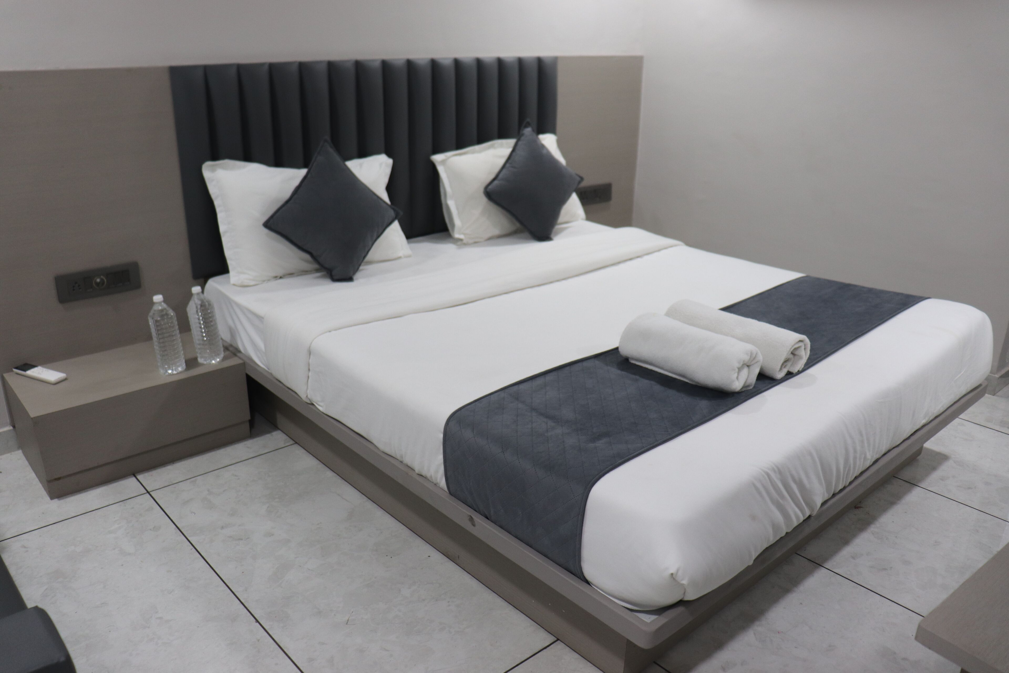 Una habitación de hotel moderna con una cama grande, una mesita de noche con un teléfono y botellas de agua, y una cama bien hecha con toallas.