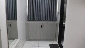 Ein Flur mit einem grauen Kleiderschrank, einem Fenster mit grauen Vorhängen und einem gefliesten Boden.
