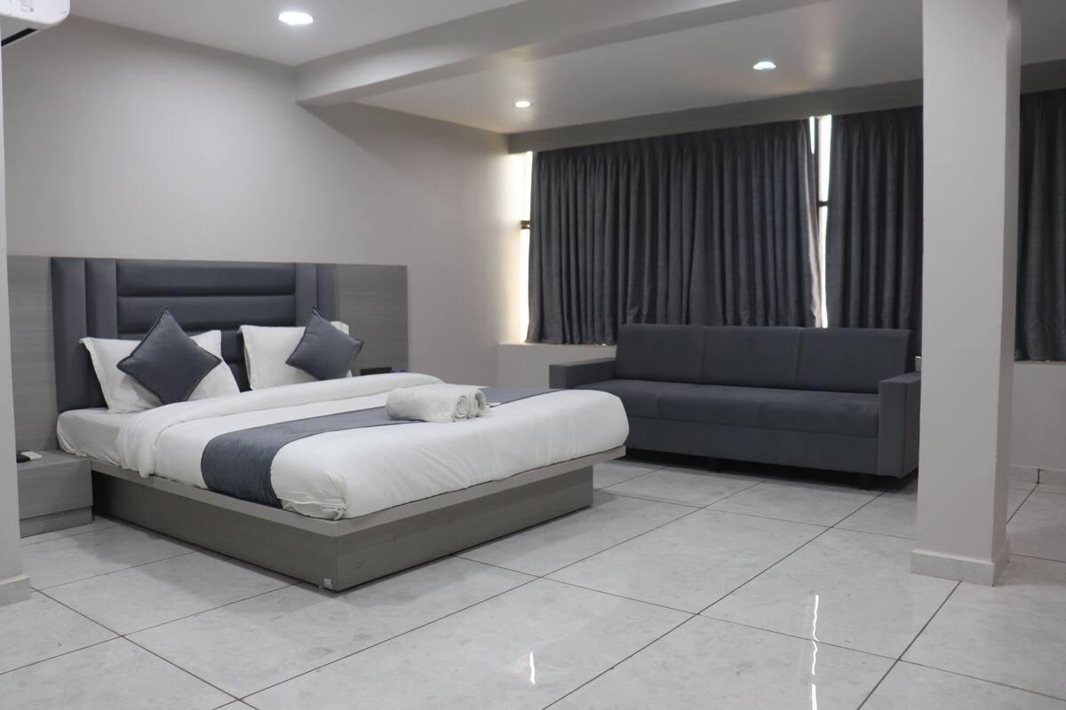 A modern bedroom with a large bed, a sofa, and a window with curtains.