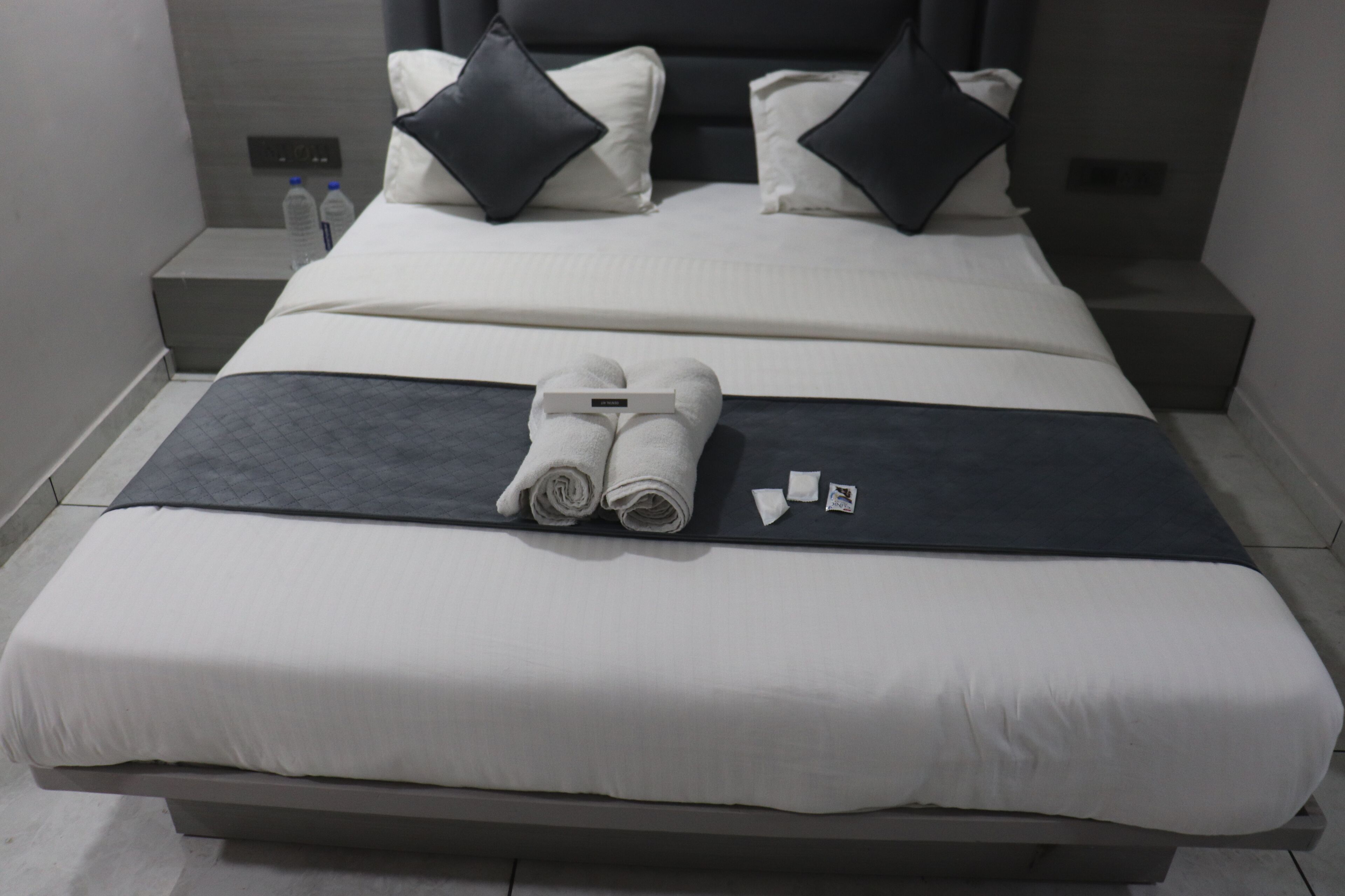 A neatly made bed with white and dark gray linens, two pillows, and a folded towel.