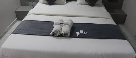 A neatly made bed with white and dark gray linens, two pillows, and a folded towel.