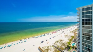 Ein Strand mit freiem Blick auf den Ozean, ein Hotelgebäude mit Balkonen und ein Poolbereich.