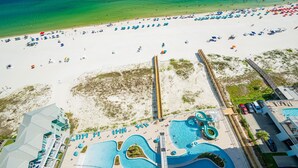 Eine Vogelperspektive auf einen Strandort mit großem Poolbereich, Strandstühlen und einer Holzpromenade.