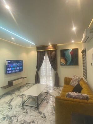 A modern living room with a flat-screen TV, a sofa, a coffee table, and a large window with curtains.