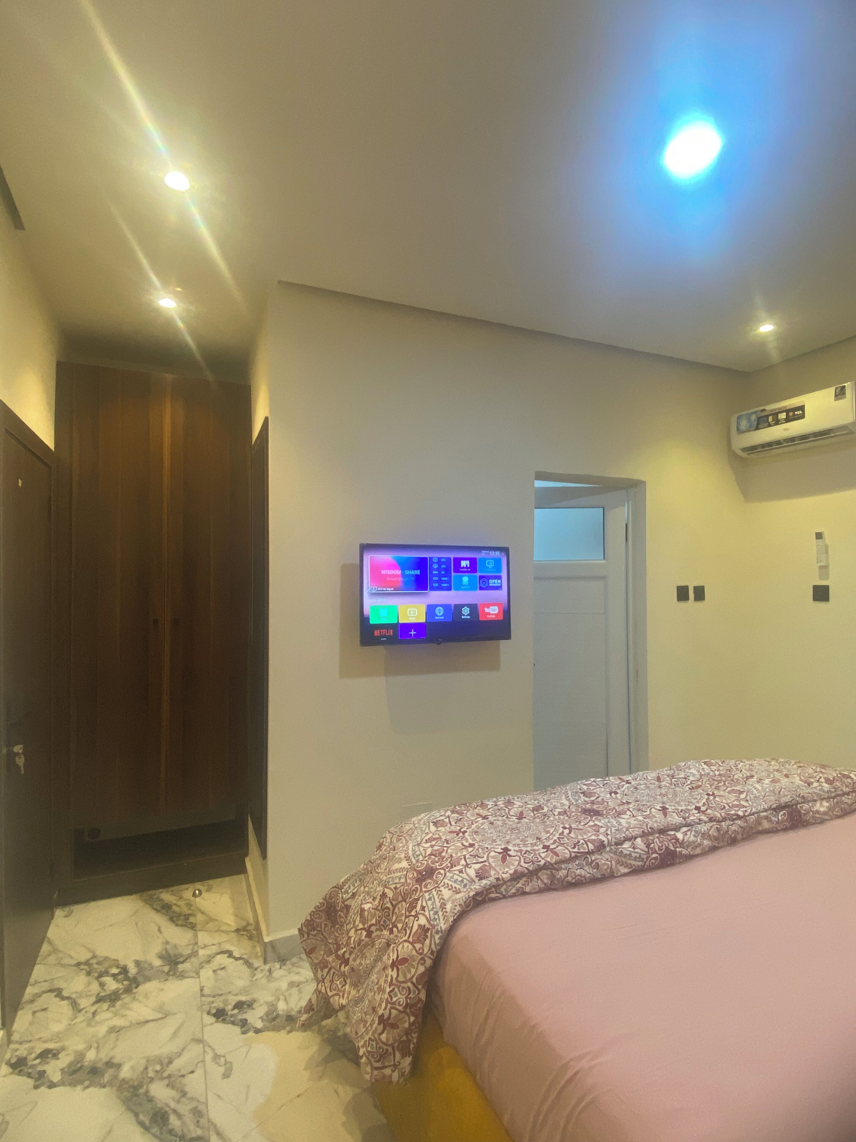 A bedroom with a bed, a TV mounted on the wall, an air conditioning unit, and a wooden wardrobe.