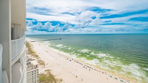 A beach with a pier extending into the ocean, a clear sky, and a balcony overlooking the scene. - Phoenix Gulf Shores Ii 2501 4 Bedroom Condo (Gulf Shores)