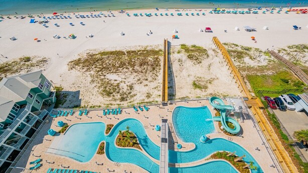 A resort with a large pool area, a beach with umbrellas, and a boardwalk.