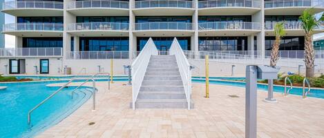 Un hotel de varios pisos con un área de piscina, que incluye una escalera que conduce a la piscina y una terraza con techo plano.