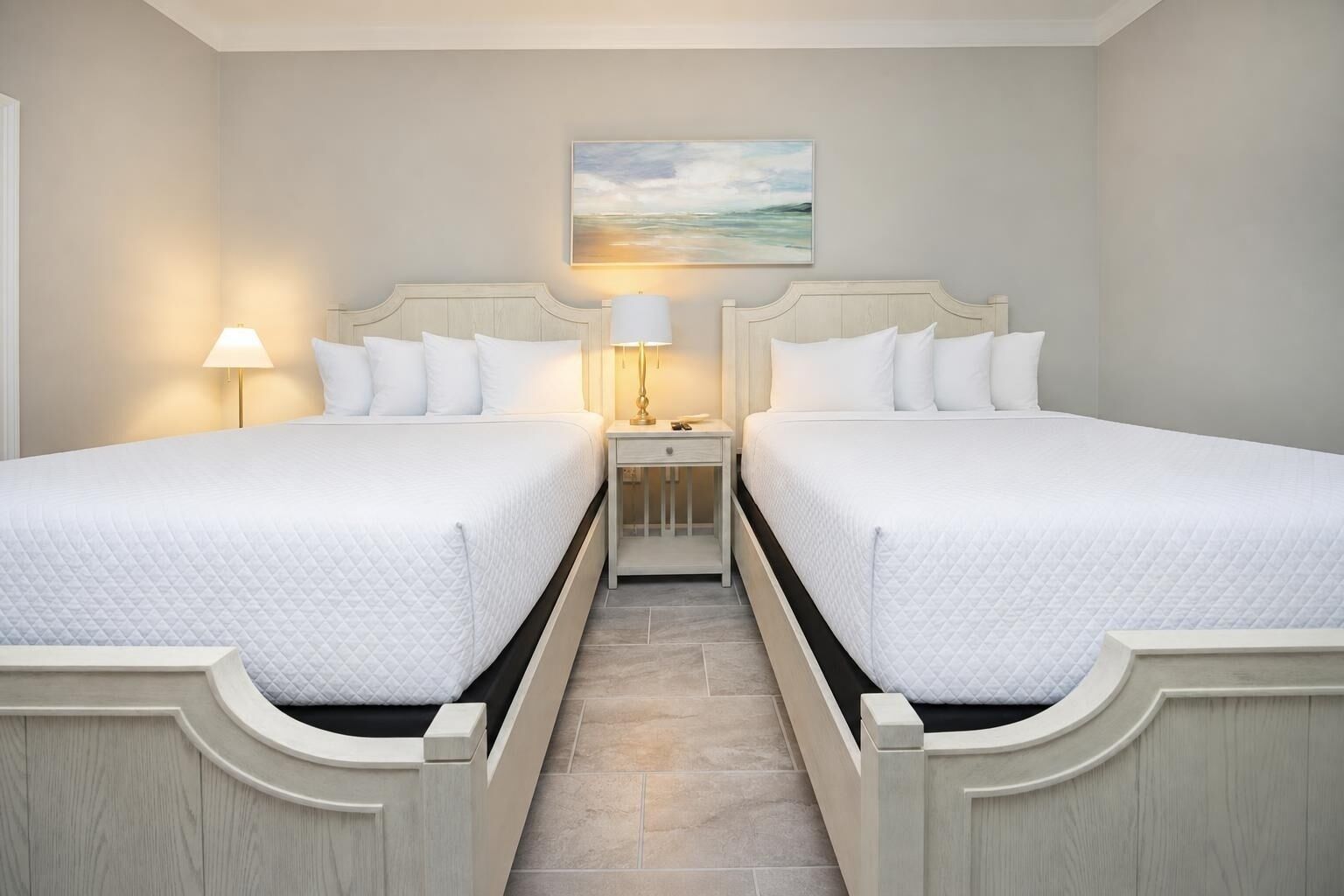 A hotel room with two beds, nightstands with lamps, a painting on the wall, and a tiled floor.