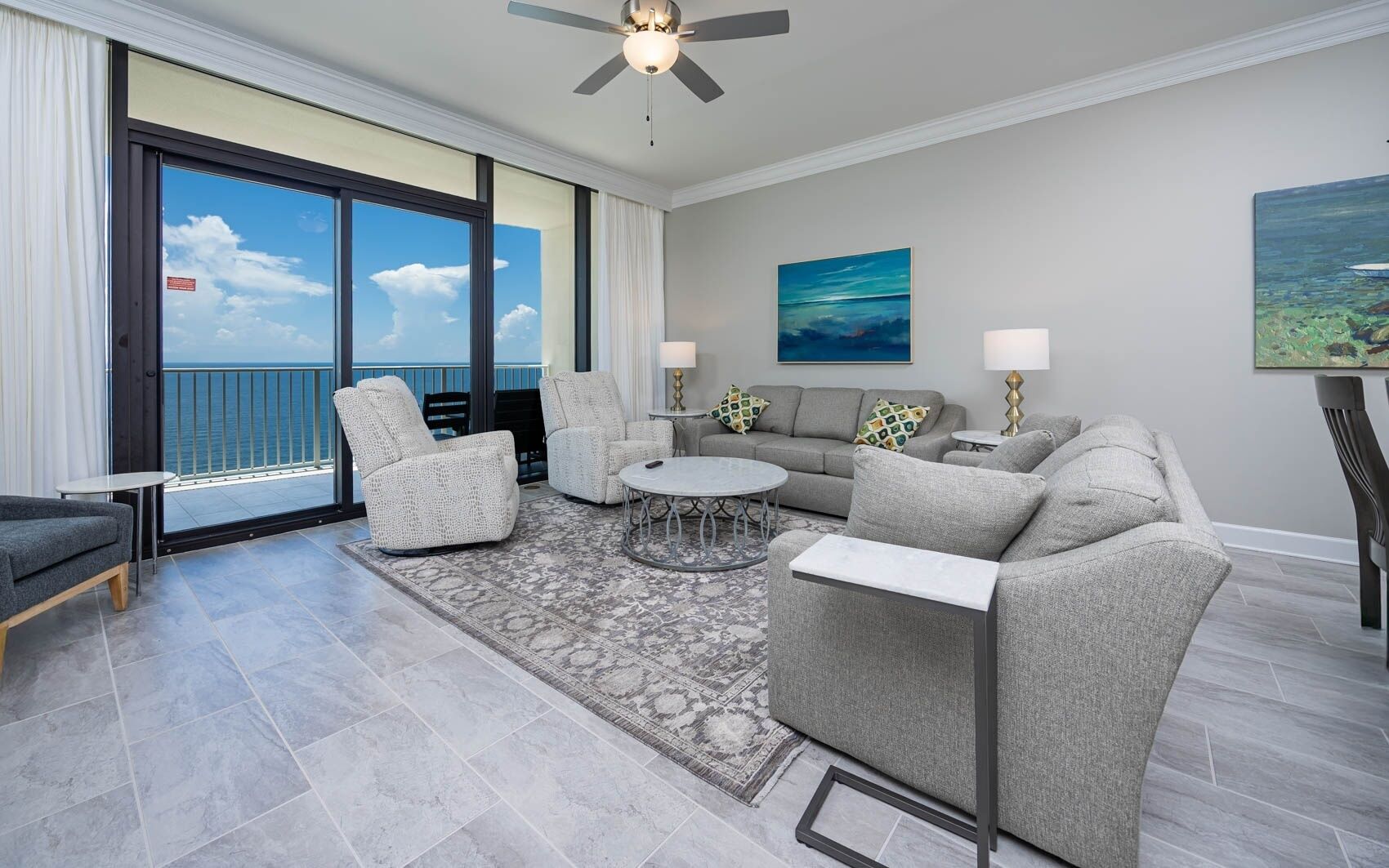 A spacious living room with a balcony, grey sofas, armchairs, and a coffee table.