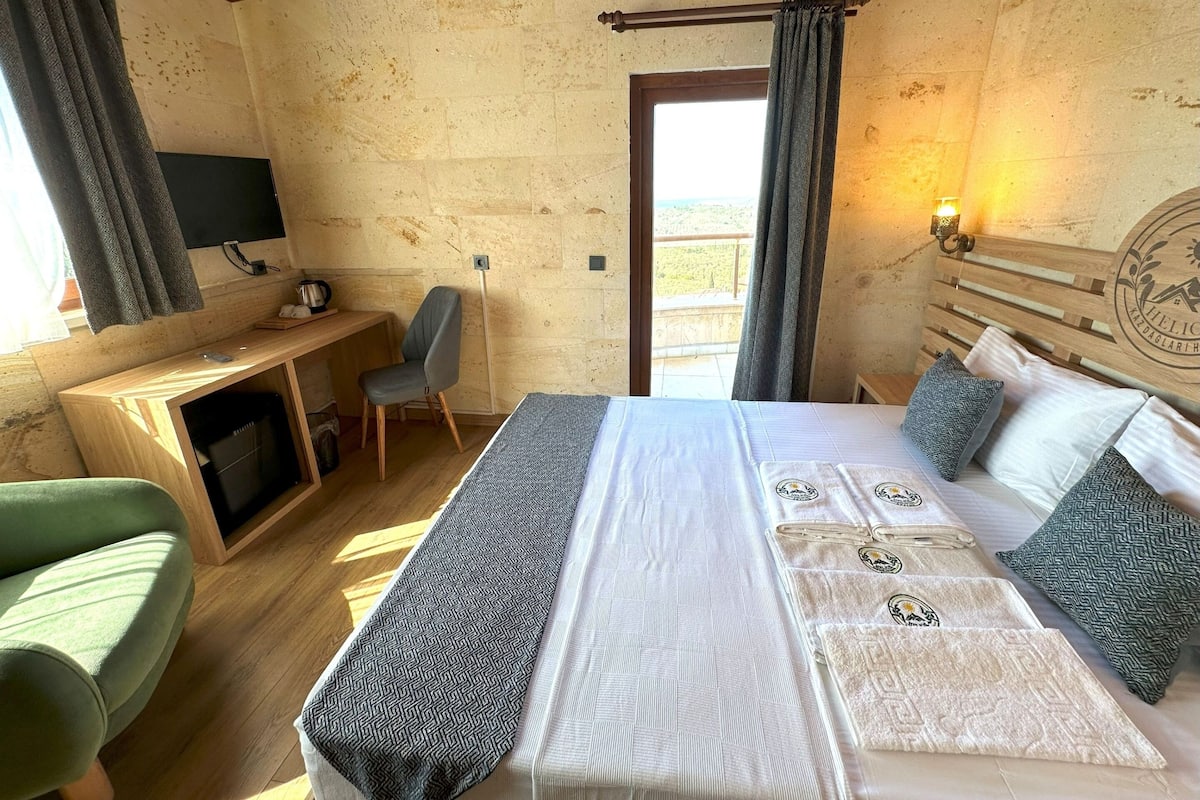 A bedroom with a bed, a desk, a chair, a TV, and a balcony view.