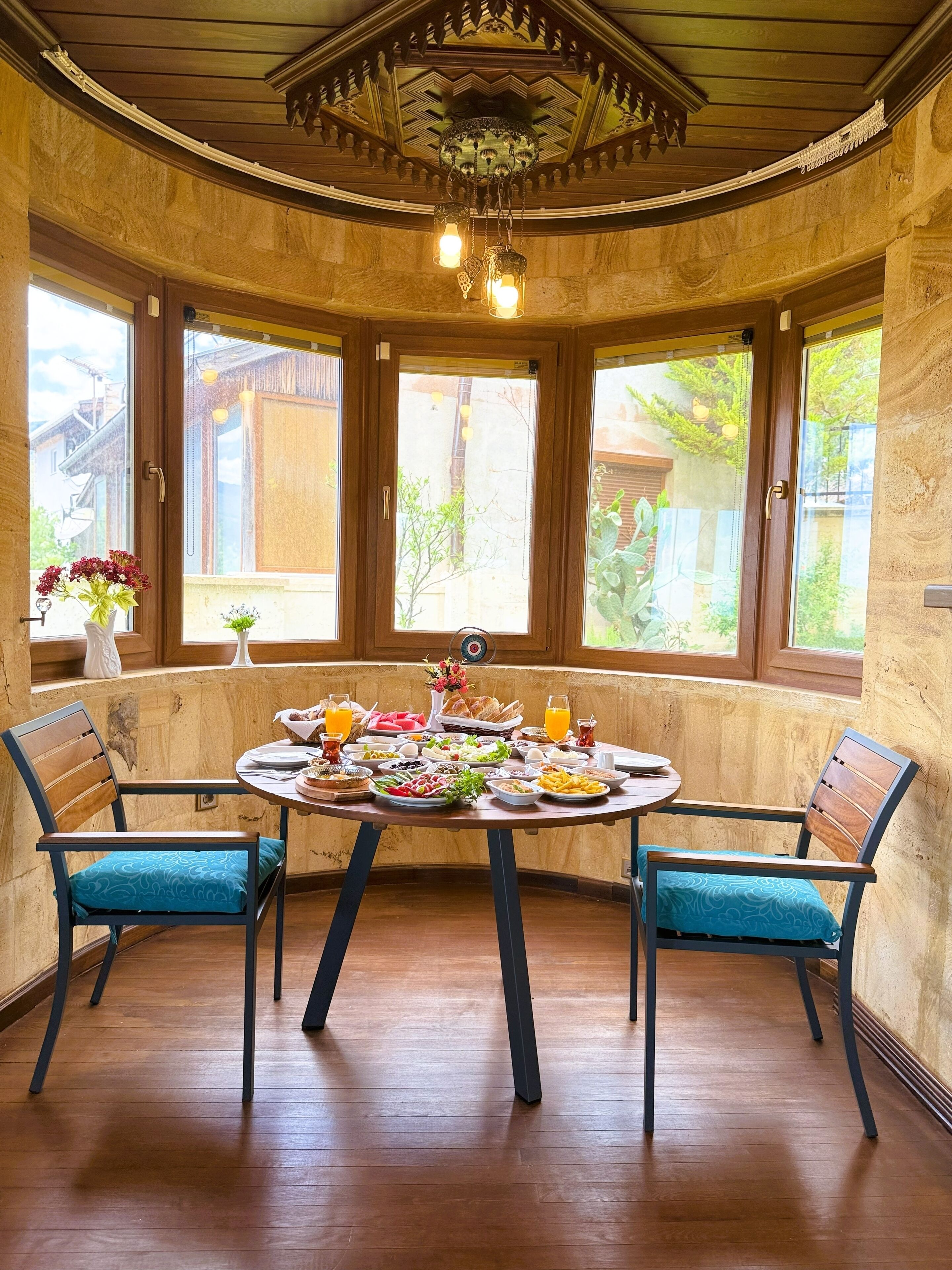 Un coin repas avec une table ronde dressée pour le repas, deux chaises et une vue dégagée sur l’extérieur grâce à de grandes fenêtres.