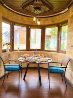 Comedor con una mesa redonda dispuesta para una comida, dos sillas y vistas amplias por las ventanas.