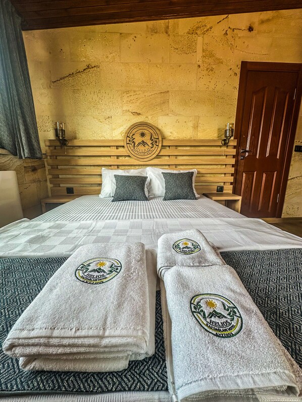 A hotel room with a bed, two pillows, a headboard, a wooden door, and a wall with a circular emblem. - Helios Kaz Dağları (Edremit)