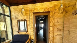 Um quarto aconchegante com uma cadeira azul-escuro, um armário de madeira e uma parede decorativa com um arco esculpido que dá para um corredor.