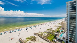 A beach with umbrellas and a pool, a clear sky, and a tall building. - Phoenix Gulf Shores Ii 1205 4 Bedroom Condo (Gulf Shores)