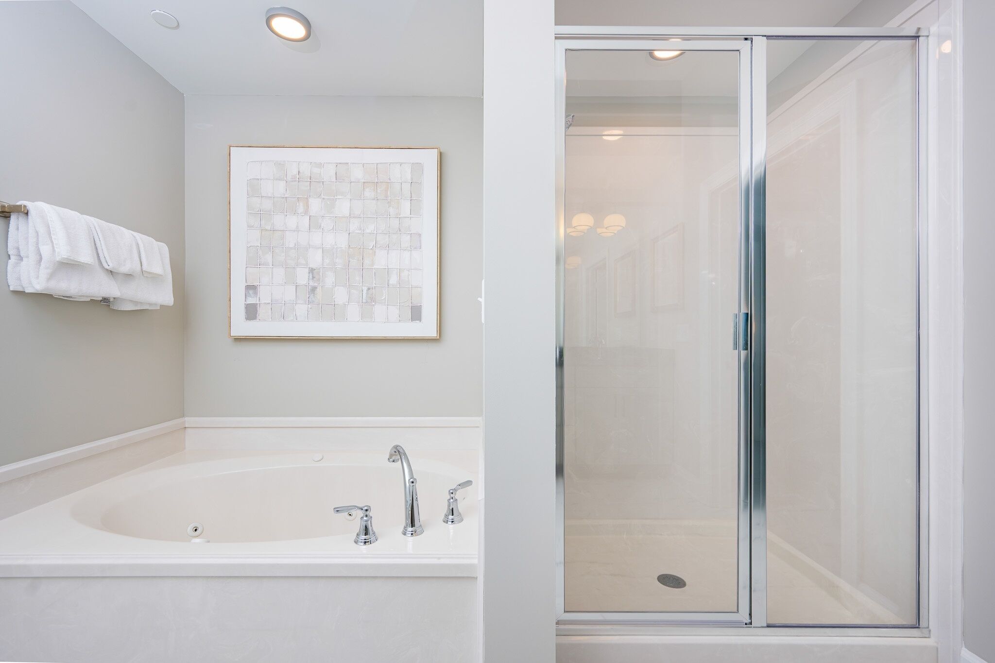 Un baño moderno con una bañera grande, una cabina de ducha de vidrio y una obra de arte enmarcada en la pared.