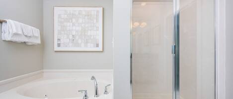 Un baño moderno con una bañera grande, una cabina de ducha de vidrio y una obra de arte enmarcada en la pared.