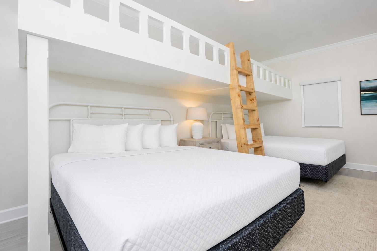 A bunk bed room with white bedding, a wooden ladder, and a nightstand with a lamp.