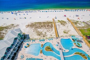 An aerial view of a beach resort with a large pool area, beach chairs, umbrellas, and a wooden boardwalk. - Phoenix Gulf Shores Ii 1104 3 Bedroom Condo (Gulf Shores)