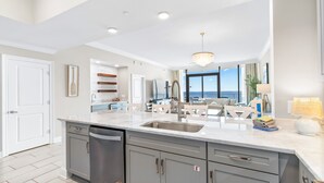 A modern kitchen with a large island, stainless steel appliances, and a view to the living area. - Phoenix Gulf Shores Ii 1502 3 Bedroom Condo (Gulf Shores)