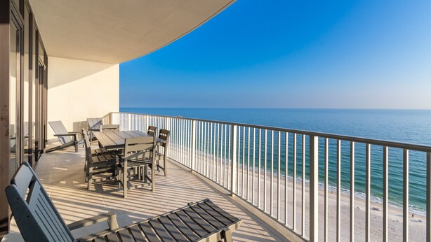 A balcony with a table and chairs, overlooking a beach and the sea. - Phoenix Gulf Shores Ii 1502 3 Bedroom Condo (Gulf Shores)