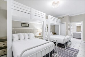 A hotel room with bunk beds, a bedside table with a lamp, a small desk, and a mirror. - Phoenix Gulf Shores Ii 1502 3 Bedroom Condo (Gulf Shores)