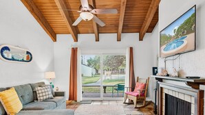 Un salon chaleureux avec une cheminée, un ventilateur de plafond et une vue sur la piscine, visible à travers la porte vitrée.