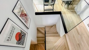Una escalera moderna con peldaños de madera y barandillas de vidrio, que baja a un nivel inferior.