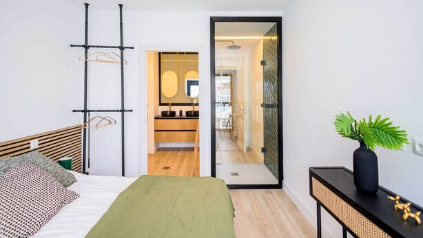 Un dormitorio moderno con una cama, una mesita de noche con una planta y vistas al baño.