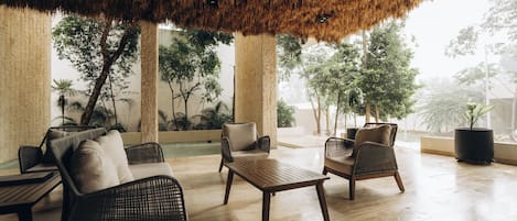 Un área de estar interior con mobiliario de mimbre, una mesa de madera y un techo de paja.