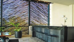 A modern bar area with a black countertop, black bar stools, and a decorative wall with diagonal lines. - NEW LISTING** This premium two-bedroom condo offers the best of both worlds - set in one of Tulum’s most desirable areas, you’re just minutes from shops, restaurants, and the main road to the beach. (Tulum)