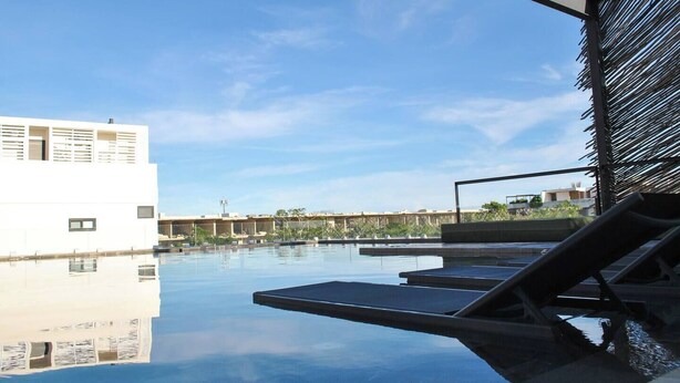 A rooftop pool with lounge chairs, a clear sky, and a modern building in the background. - NEW LISTING** This premium two-bedroom condo offers the best of both worlds - set in one of Tulum’s most desirable areas, you’re just minutes from shops, restaurants, and the main road to the beach. (Tulum)