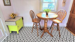 Un comedor con una mesa redonda de madera, dos sillas de madera, un mueble pequeño verde y una cortina floral sobre una ventana.