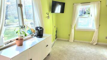 A room with a large window, a flat-screen TV, a coffee maker, and a potted plant.